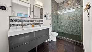 Une salle de bain moderne avec un grand miroir, deux lavabos, des toilettes et une douche à parois de verre.