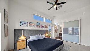 Une chambre moderne avec un grand lit, un ventilateur de plafond et des œuvres d’art accrochées au mur.