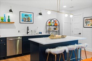 Een moderne keuken met een centraal eiland, roestvrijstalen apparatuur en een decoratieve plank met kleurrijk glaswerk.