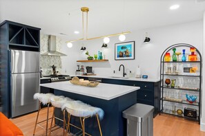 Een moderne keuken met een centraal eiland, roestvrijstalen apparatuur en een decoratieve plank met glazen.