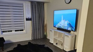 A living room with a flat-screen TV, a clock, and a large black rug. - Cozy clean, family sized house. (Cambridge)