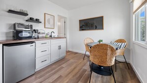 Eine moderne Küche mit Geschirrspüler, einer Kaffeemaschine und einem Essbereich mit Korbstühlen und einem Tisch.