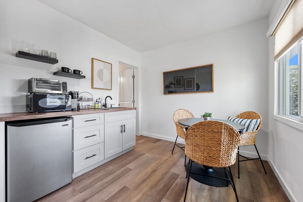 A modern kitchen with a built-in dishwasher, a coffee machine, and a dining area with wicker chairs and a table.