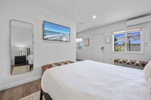 A bedroom with a large bed, a TV mounted on the wall, a window with an umbrella, and a door.