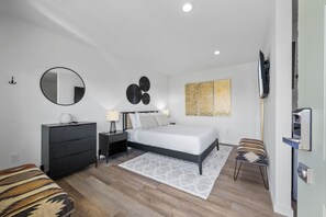 Un dormitorio moderno con cama, cómoda, mesitas de noche y televisor.
