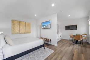 A bedroom with a bed, a desk, and a chair, a bathroom with a shower, and a living area with a TV.