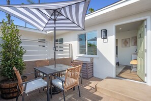 Un espace patio aménagé avec une table et des chaises, un parasol à rayures et une plante en pot.