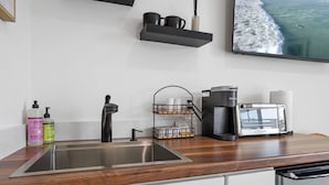 Een moderne keuken met een RVS spoelbak, een koffiezetapparaat, een broodrooster en een plank met kopjes en een vaas.
