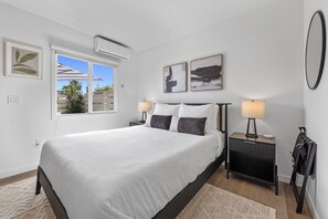 Une chambre à coucher avec un lit, des tables de chevet, une lampe, un miroir et des œuvres d’art accrochées aux murs.