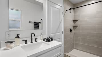 Un baño moderno con un tocador blanco, un espejo grande, un perchero y una ducha con grifo negro, además de paredes de ducha con azulejos.