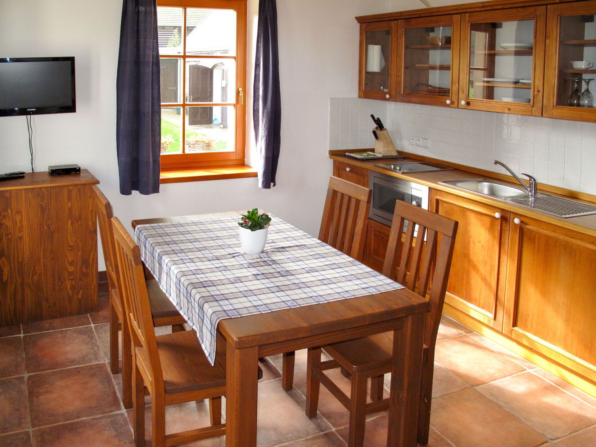 Une cuisine compacte avec des meubles en bois, une table à manger avec des chaises, un petit four et un téléviseur posé sur un meuble en bois.