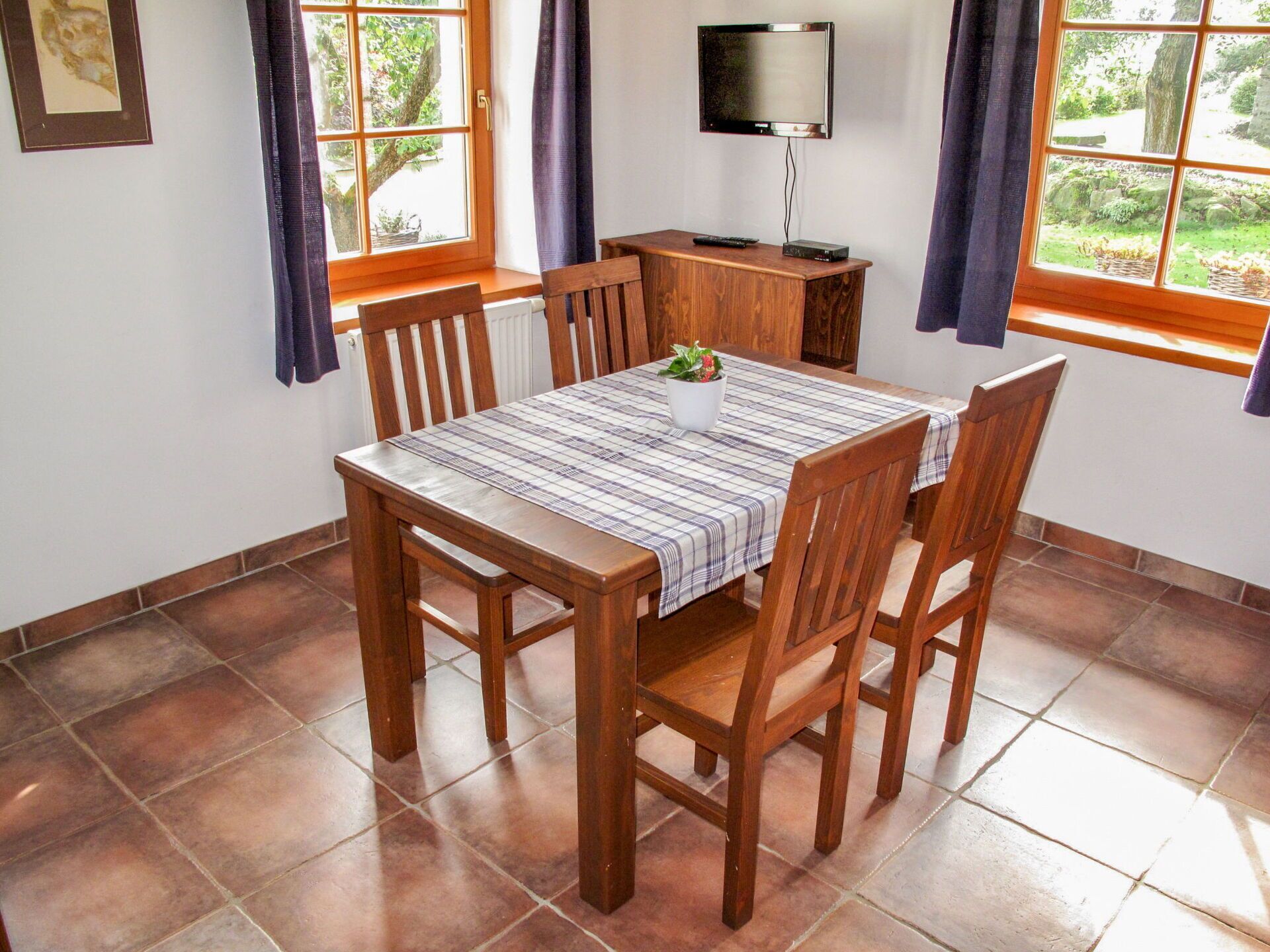 Un comedor con una mesa y sillas de madera, un televisor sobre un mueble bajo y una ventana con cortinas.