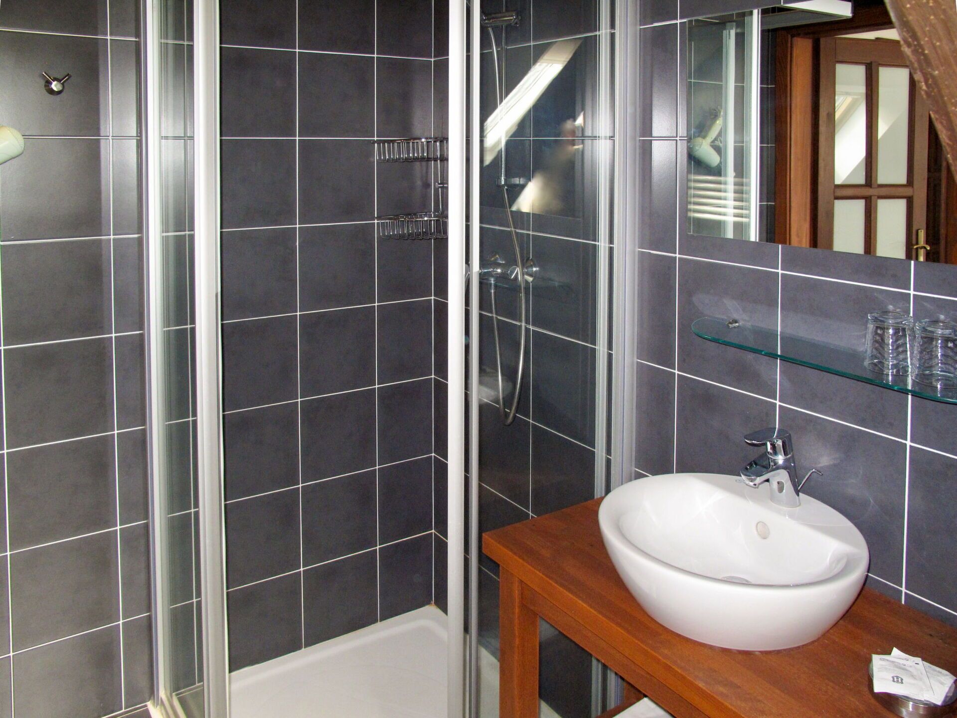 Ein Badezimmer mit Duschkabine aus Glas, einem weißen Waschbecken und einem Holzbadezimmerkorpus.