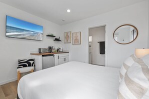 Ein Schlafzimmer mit einem großen Bett, einer Küchenzeile mit einem Toaster, einem Stuhl und einem Bild von einer Strandansicht.