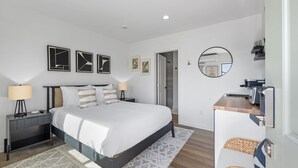 A modern bedroom with a large bed, bedside tables, a mirror, and artwork on the wall. - South Oceanside Bungalow 5 - Deluxe Queen Studio + Patio (Oceanside)
