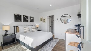 Une chambre à coucher moderne avec un grand lit, des tables de chevet, un miroir rond et des œuvres d’art accrochées aux murs.