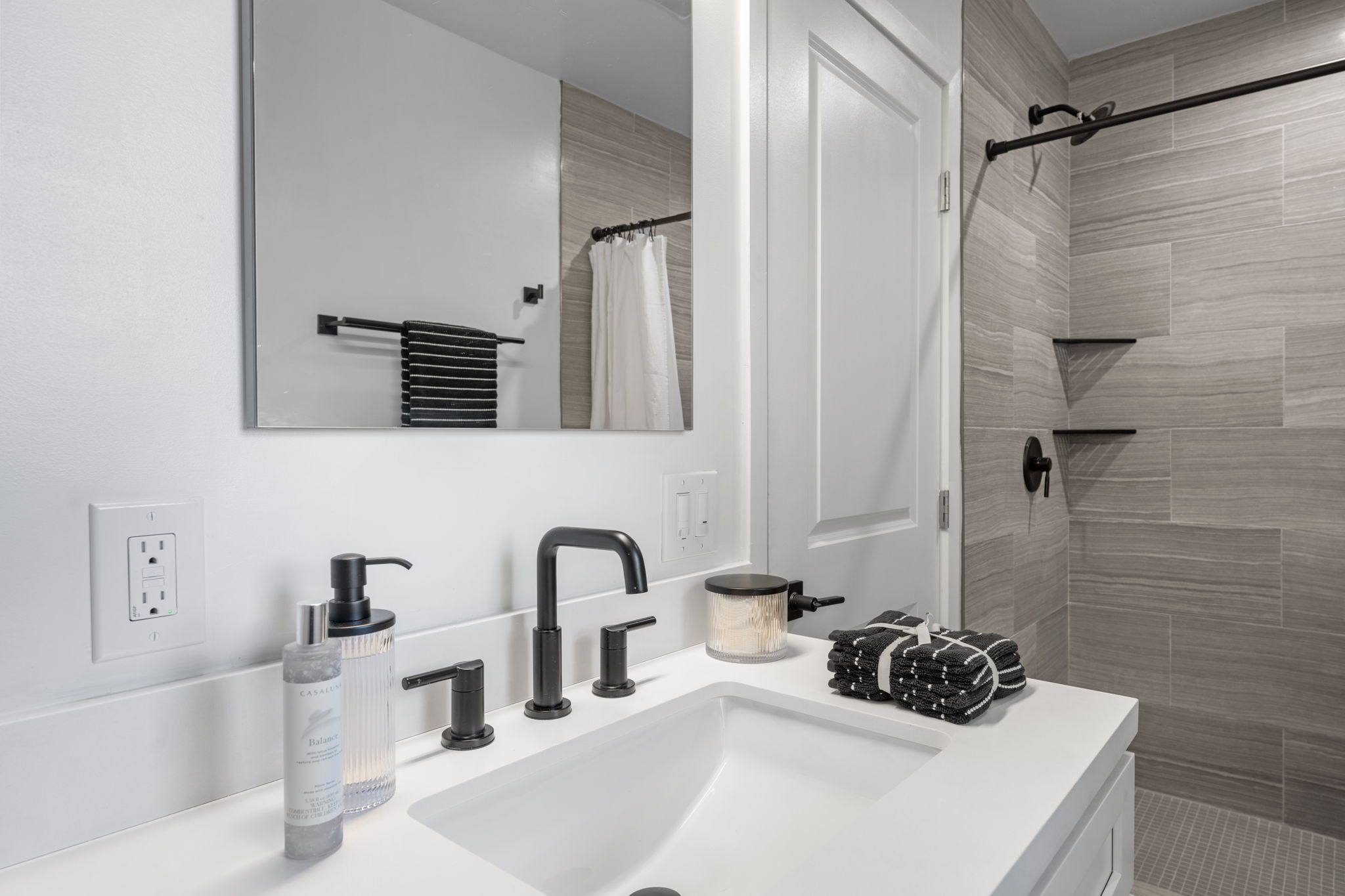 A modern bathroom with a white sink, black faucets, a mirror, and a towel rack.