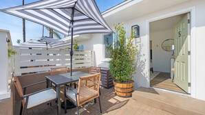 An outdoor patio with a table and chairs, a striped umbrella, and a potted plant. - South Oceanside Bungalow 5 - Deluxe Queen Studio + Patio (Oceanside)