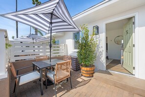 Un patio con una mesa, sillas, un paraguas a rayas y una planta en maceta.