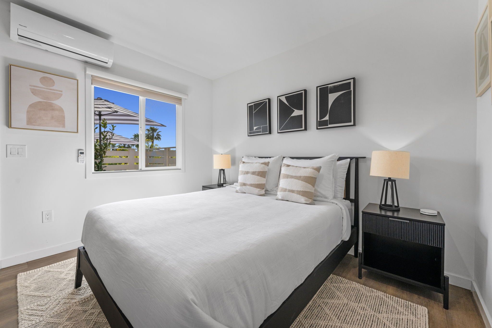 A bedroom with a large bed, two bedside tables with lamps, a window with a view, and wall-mounted artwork.