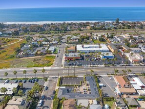 Vista aérea de un pueblo costero con un puerto deportivo, un edificio comercial grande y zonas residenciales.