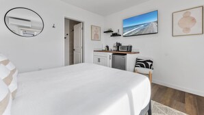 Une chambre avec un lit, un coin cuisine, une salle de bain et une grande fenêtre donnant sur la plage.