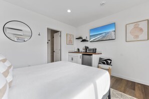 Un dormitorio con cama, kitchenette, baño y ventana grande con vista a la playa.