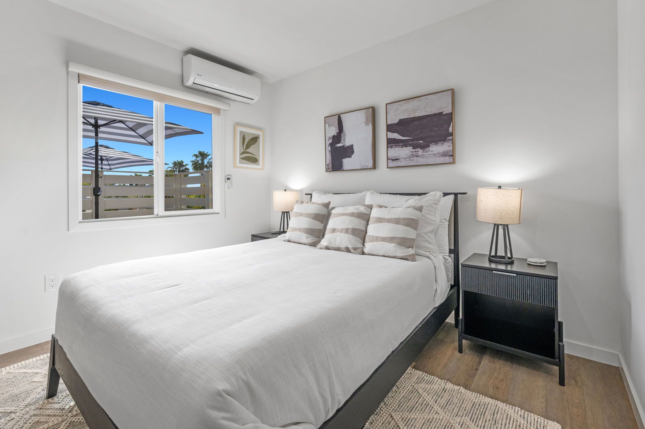 Un dormitorio con una cama, dos mesitas de noche, una ventana y un aire acondicionado instalado en la pared.