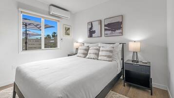 Un dormitorio con una cama, dos mesitas de noche, una ventana y un aire acondicionado instalado en la pared.