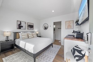 Een moderne slaapkamer met een bed, nachtkastjes, een bureau en een televisie.
