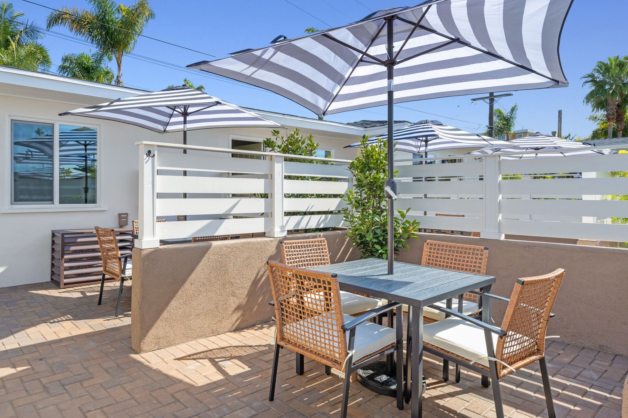 An outdoor patio with a table and chairs, surrounded by white fences and palm trees.