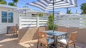 Une terrasse extérieure avec une table et des chaises, entourée de clôtures blanches et de palmiers.
