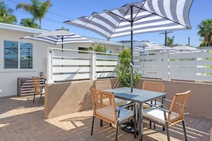 Une terrasse extérieure avec une table et des chaises, entourée de clôtures blanches et de palmiers.