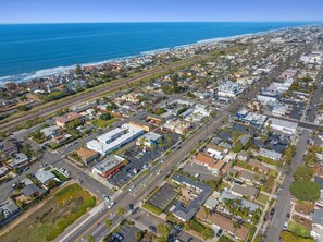 Vue aérienne d’une ville côtière, avec un mélange de bâtiments résidentiels et commerciaux, une station-service bien visible et une plage en arrière-plan.