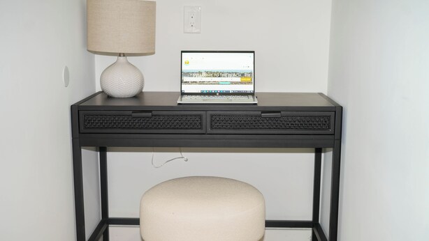 Un bureau avec un ordinateur portable, une lampe et un tabouret rembourré.