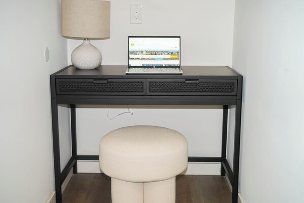 Un bureau avec un ordinateur portable, une lampe et un tabouret rembourré.