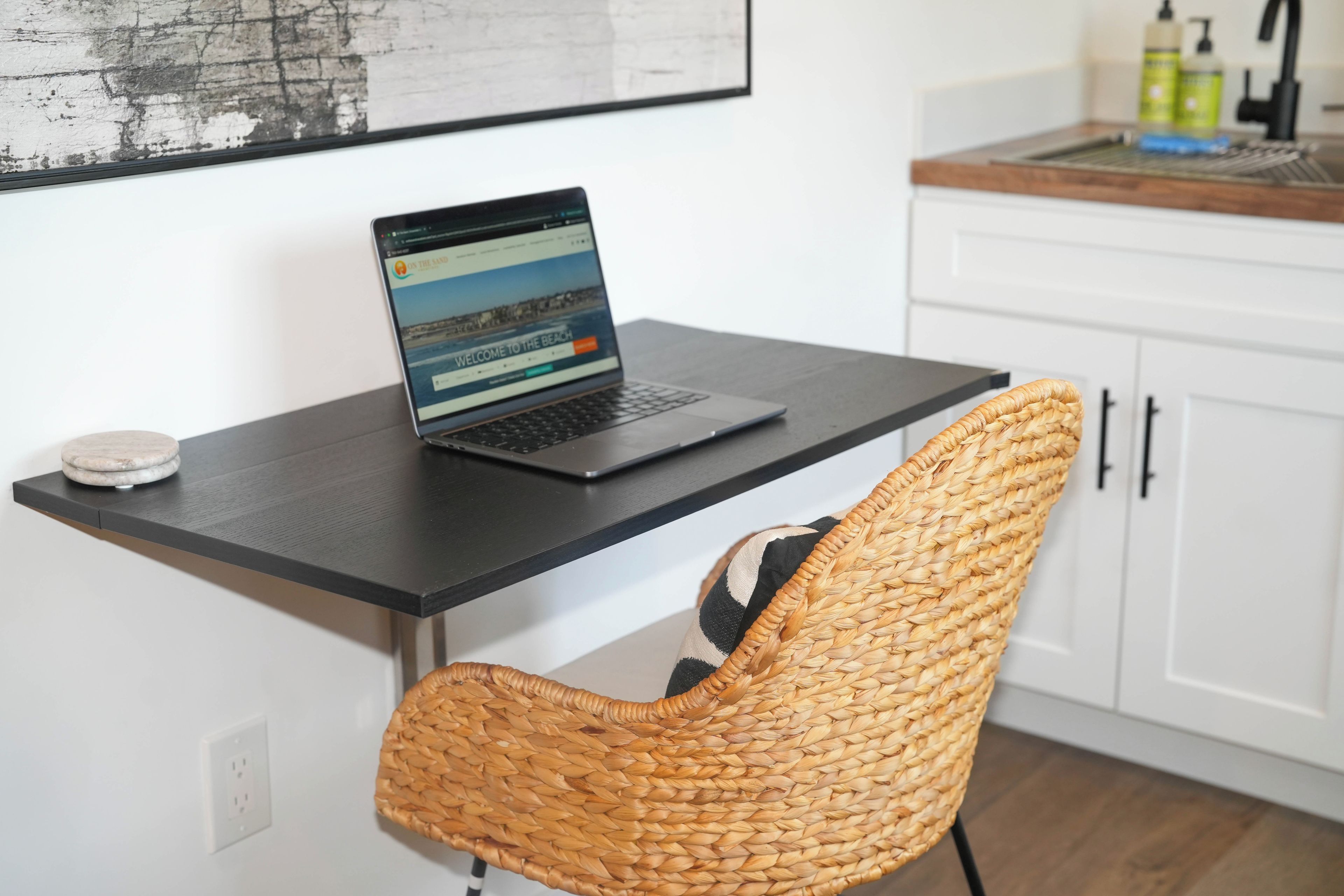 A laptop on a black desk with a woven chair in front.