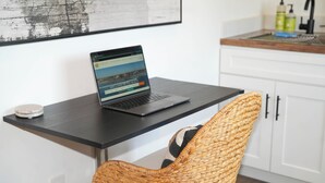 Een laptop op een zwart bureau, voor een geweven stoel.