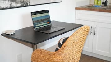 A laptop on a black desk with a woven chair in front.