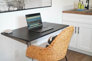 Een laptop op een zwart bureau, voor een geweven stoel.