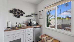 A compact kitchen with a dishwasher, a coffee maker, and a window overlooking a patio. - South O Bungalow 9 - Deluxe Work and Stay Queen Studio + Patio (Oceanside)