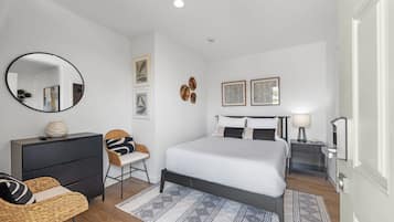 A modern bedroom with a large bed, a round mirror, a dresser, and a chair.