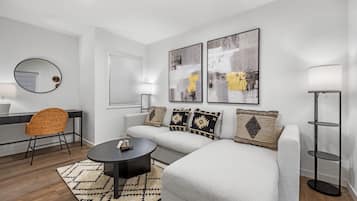 A modern living room with a sofa, a round coffee table, a wicker chair, a floor lamp, and abstract wall art.