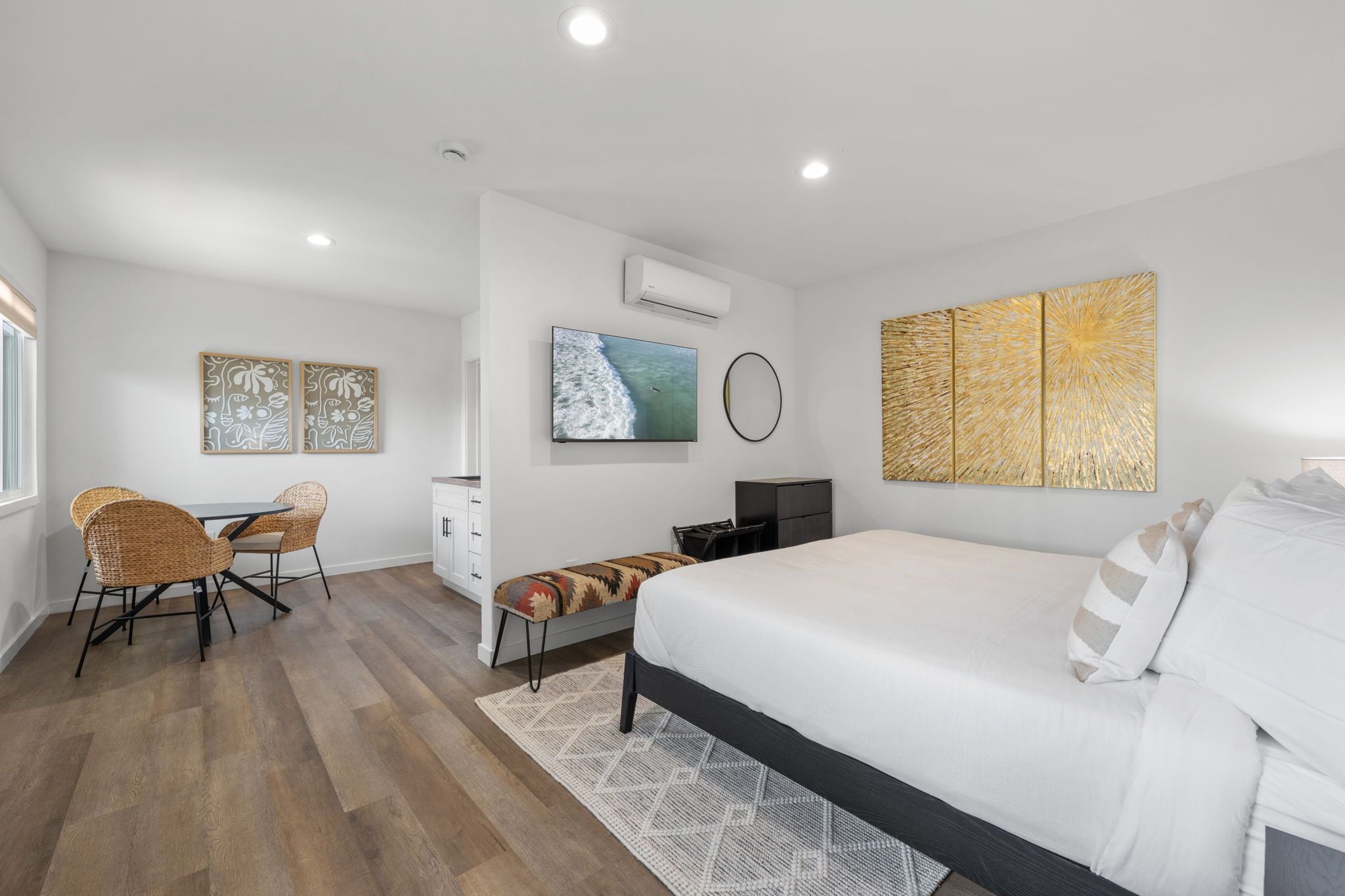A modern bedroom with a bed, a desk, and a chair. There is a TV mounted on the wall and artwork above it.