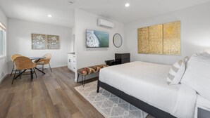 Une chambre moderne avec un lit, un bureau et une chaise. Un téléviseur est fixé au mur, et une œuvre d’art est accrochée au-dessus.