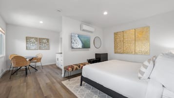 A modern bedroom with a bed, a desk, and a chair. There is a TV mounted on the wall and artwork above it.