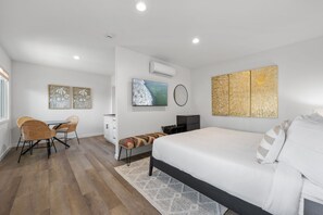 Un dormitorio moderno con cama, escritorio y silla. Hay un televisor montado en la pared y una obra de arte encima.