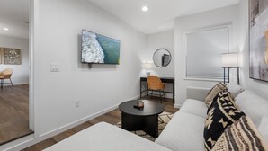 Un salon moderne avec un téléviseur à écran plat, une table basse ronde, un canapé et une fenêtre équipée de stores.