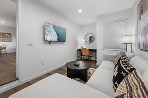 Una sala de estar moderna con televisor de pantalla plana, una mesa redonda, un sofá y una ventana con persianas.
