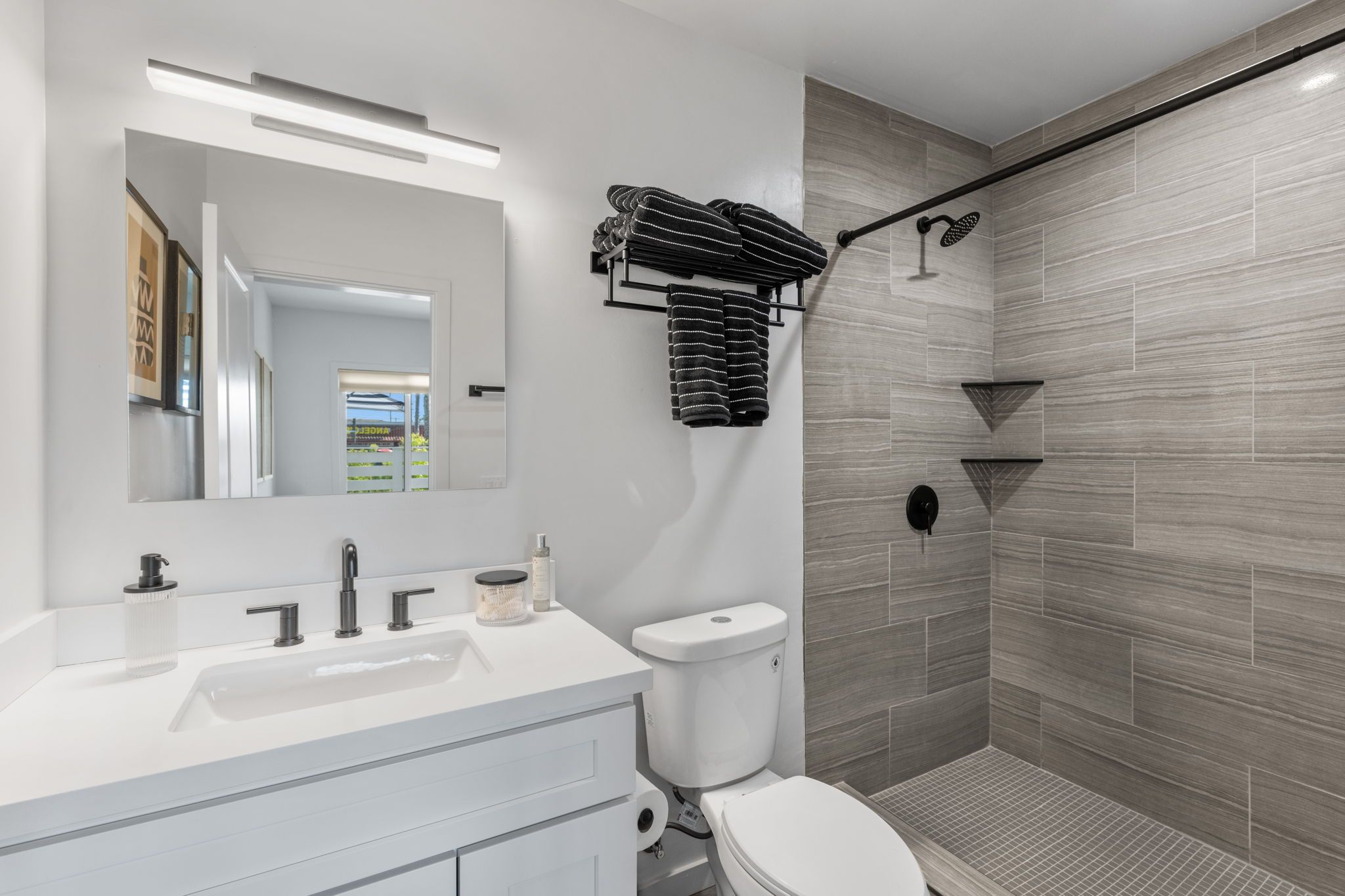 A modern bathroom with a white vanity, a toilet, a shower with a glass door, and a towel rack with folded towels.